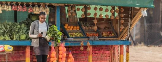 lady using phone in front of vegetable stand